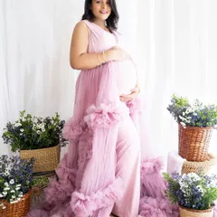 A beautiful solo shot of a mom-to-be in a ruffled pink gown, surrounded by baskets of flowers in a bright, airy studio.