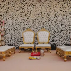 Elegant gold and white throne-like seating for the bride and groom, set against a dense backdrop of white carnations for a truly royal wedding ceremony.