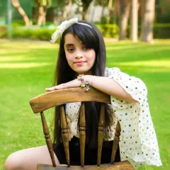 A young girl poses confidently with a wooden chair in a green, sunny park. A beautiful and classic outdoor portrait.
