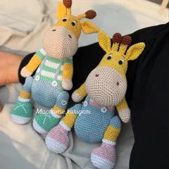 Our amigurumi giraffes, Tinu and Minu, sitting pretty. One wears overalls and the other a striped shirt, showcasing how we can customize outfits and details to give each toy its own personality.