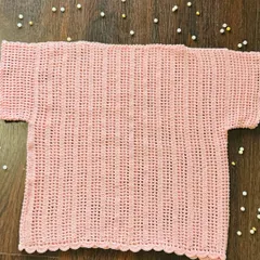 A flat-lay view of the baby pink kids' top. You can see the delicate scalloped hem and the consistent vertical stitching I use to create this simple, airy design.