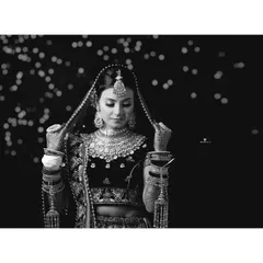An elegant black and white portrait of the bride adjusting her dupatta. The soft bokeh in the background and the focus on her intricate jewelry create a classic and graceful image.