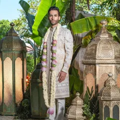 A groom's welcome, framed by tradition and nature. This full-length view of an ivory sherwani, adorned with a floral garland, highlights the garment's majestic presence, perfect for the grand entrance.