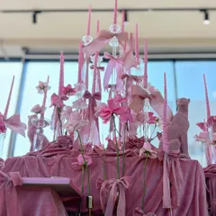 A close-up of the centerpiece for the pink-themed event, featuring tall pink candles, velvet ribbons, and a miniature pink panther statue, all set on a bed of draped pink velvet.