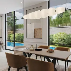 This open-plan living and dining area in a Goa villa overlooks the pool through floor-to-ceiling windows. The design uses a neutral palette, natural materials, and modern lighting to create a seamless transition between indoors and outdoors.