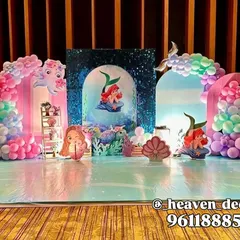 An elaborate stage setup for a Little Mermaid party, creating an under-the-sea kingdom. The design uses multiple backdrops, including a sequin panel, and pastel balloon arches to mimic ocean waves.