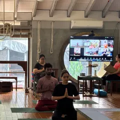 A hybrid class in session, with students practicing both in person and online. This image shows the focus and dedication of the group as they begin their practice with a moment of quiet centering.