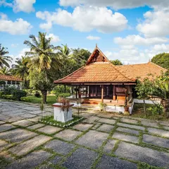 A wide, sunlit view of the Aranmula Palace courtyard. The expansive stone-paved ground and the traditional architecture under a bright sky showcase the scale and beauty of our main reception building.
