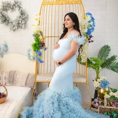 A portrait of a queen on her throne. Seated in our popular golden birdcage chair, this mother-to-be looks radiant in a light blue ruffled gown, surrounded by delicate floral arrangements.