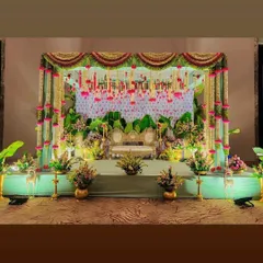A full view of a baby shower stage decoration. The setup includes a traditional throne, a banana leaf backdrop, and beautiful hanging flower arrangements.