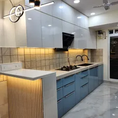 This is a real-site photograph of a parallel modular kitchen we delivered. It features a dual-tone acrylic finish with powder blue and white cabinets, a breakfast counter with fluted paneling, and under-cabinet lighting for a functional and stylish cooking space.