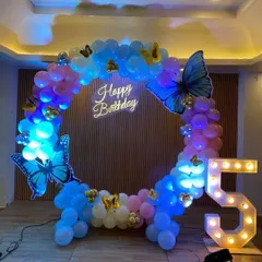 This circular balloon arch with large butterfly cutouts and a 'Happy Birthday' neon sign is perfect for a magical birthday party. The light-up number '5' adds to the charm.