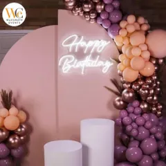 A stylish birthday backdrop with a pastel pink arch, a custom "Happy Birthday" neon sign, and an organic balloon garland in muted tones.