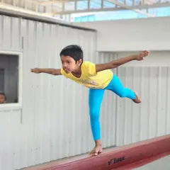 A young student demonstrates excellent balance and posture while practicing a pose on the gymnastics beam.
