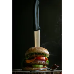 A gourmet chicken burger presented with a knife, set against a dark, smoky background. This dramatic styling gives the burger a bold and premium feel for a restaurant menu.