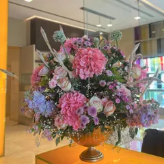 A large, opulent floral arrangement in a gold urn, featuring a mix of pink hydrangeas, roses, and other seasonal blooms. This statement piece added a touch of grandeur to the restaurant's decor.