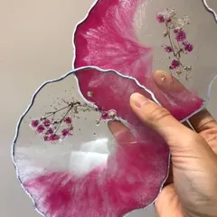 These geode-style resin coasters feature a striking pink and white swirl design with delicate sprigs of baby's breath preserved within the clear resin.