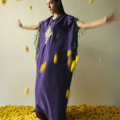 A dynamic shot for a Vogue editorial, capturing a model in a purple kaftan surrounded by falling marigold flowers. The styling uses motion and color contrast to create a vibrant and expressive image that blends traditional elements with contemporary fashion.