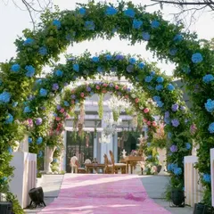 The entrance to the ceremony area, featuring a pink carpet runner leading through a series of lush floral arches in shades of blue, pink, and purple.