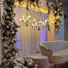 A romantic Roka ceremony setup with a plush velvet sofa, elegant chandeliers, and pillars adorned with cascading pastel roses.