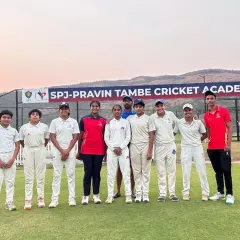 A group photo of our women's team with their coaches on our home ground, with the official SPJ-Pravin Tambe Cricket Academy banner in the background.