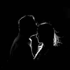 A striking black and white portrait using rim lighting to outline the couple's features against a dark background.