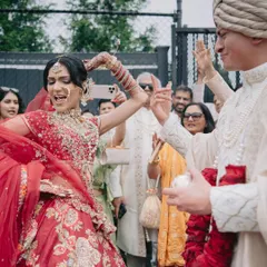 The joy of the baraat! The bride, in her stunning red lehenga, dances with her groom, who is styled in a classic ivory sherwani, creating a timeless and energetic look.