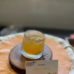 The vibrant 'Mango Tango' mocktail, beautifully presented in a modern glass on a wooden coaster. We pay attention to every detail, including the presentation of our drinks.