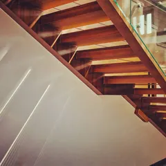 We believe architecture comes alive with light. This photograph captures the deliberate play of light and shadows across a wooden staircase, turning a simple transitional space into a moment of abstract beauty.
