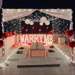 I designed this romantic rooftop proposal within a fairy light cabana. The setup includes low floor seating for an intimate dinner, heart-shaped foil balloons, and glowing 'MARRY ME' marquee letters as the centerpiece.