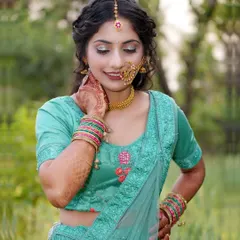 A beautiful portrait taken in a natural, green setting. The model's teal lehenga and traditional jewelry stand out, while her gentle pose conveys a sense of peace and elegance.