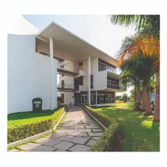 The entrance to the office building is marked by a large, double-height volume supported by slender columns. This creates a welcoming, shaded transition space, with a stone pathway leading through landscaped gardens.