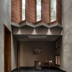 The entrance foyer of the Brick House sets a contemplative tone. Fluted concrete walls, black stone flooring, and strategically placed brickwork create a rich textural experience, animated by light from the staggered windows above.