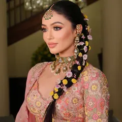 A beautiful close-up of a bride with a thick, long braid woven with fresh, colorful flowers. This is a perfect hairstyle for a Mehendi or Haldi ceremony, adding a natural and joyful element to the look.