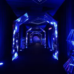 Another view of the electric blue entrance tunnel, with a neon sign and floral stands at the end, guiding guests toward the main event space.