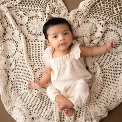 A simple and sweet portrait of a baby girl lying on a heart-shaped crochet blanket. Her direct gaze and cute outfit make this a lovely milestone photo.