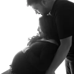 A tender moment captured in silhouette. The dad-to-be kisses his partner's forehead, a gesture of love and support that is beautifully conveyed through their shadows.