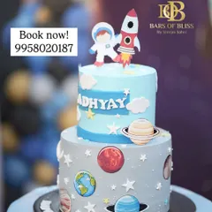 A two-tiered space exploration cake perfect for a young astronaut's birthday. The design features edible planets, stars, a rocket ship, and an astronaut, creating an out-of-this-world celebration centerpiece.