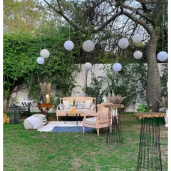 A wider angle of the boho-chic lounge, showing how it integrates into the natural garden setting. The hanging paper lanterns in the trees add a touch of magic to the space.
