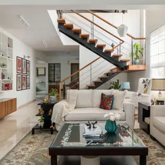 The interconnected living, dining, and stairway area in the 'House of Kismish' creates a grand, open feel. We designed this formal living space for conversation, which transitions into a cozy reading nook under the high ceiling, perfect for moments of solitude.