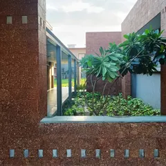 A view through a window-like opening at the Bagchi Karunashraya hospice in Bhubaneswar. The laterite stone walls frame a small, private courtyard, creating a moment of quiet connection with nature.