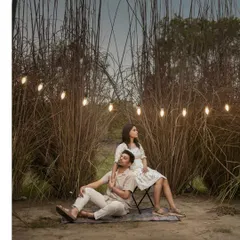 A beautifully lit outdoor evening shot. The string lights create a warm, magical glow around the couple, perfect for a romantic and whimsical pre-wedding theme.