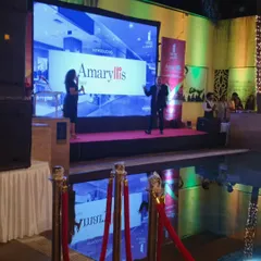A poolside product launch for 'Amaryllis'. The setup includes a stage with a large LED screen for the presentation, professional lighting, and a roped off VIP area.