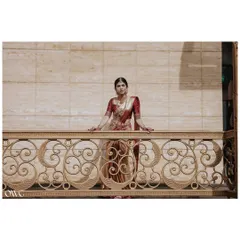 A wide, cinematic portrait of the bride on an ornate balcony, looking like royalty in her traditional red and gold saree.