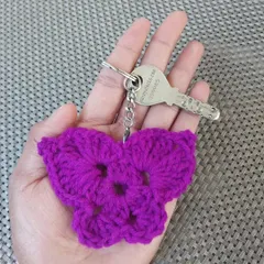 A vibrant magenta butterfly keychain held in my hand to show its size. It's a lightweight and beautiful accessory.