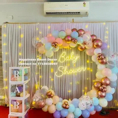 This modern baby shower setup is very popular. It features a full ring backdrop covered in a garland of pastel and metallic balloons, a 'Baby Shower' neon sign, and transparent 'BABY' boxes filled with matching balloons.