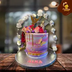 A fairy-themed cake that looks like it came from an enchanted garden. It features a beautiful watercolor buttercream finish, gold drips, and is topped with fresh flowers, a fairy, and butterflies.