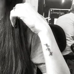 A black and white shot of a delicate 'Ant asti prarambh' script tattoo on the wrist, showcasing its elegant placement.