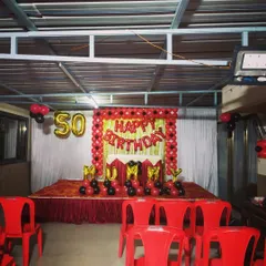 A classic red and black stage decoration for a 50th birthday party. The setup includes a balloon frame, 'MUMMY' foil letters, and seating arrangements for guests.