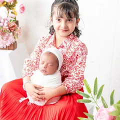 A proud big sister holds her newborn sibling for the first time. This heartwarming shot captures the beginning of a lifelong bond, set against a soft floral background.